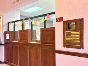 Braille American Flag and commemorative plaque mounted on a wall inside Abbeville City Hall, displayed near the public counter so visitors can see and touch the tactile flag.