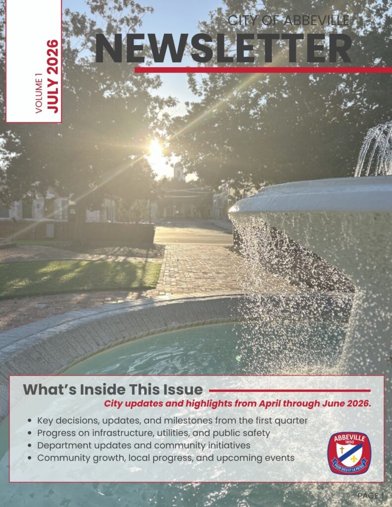 Cover of the City of Abbeville Newsletter, Volume 1, July 2026. The cover features a photograph of the fountain in Magdalen Square with morning sunlight shining through large oak trees and historic downtown Abbeville visible in the background. The title "City of Abbeville Newsletter" appears across the top. A panel at the bottom previews the issue, highlighting city updates and accomplishments from April through June 2026, including key decisions and milestones, infrastructure and public safety progress, department updates and community initiatives, and community growth, local progress, and upcoming events. The City of Abbeville seal appears in the lower right corner.